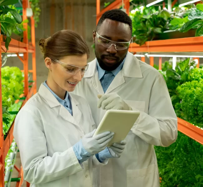 Nephsonic_smiling-young-interracial-greenhouse-engineers-lab-coats-protective-goggles-using-tablet-while-maintaining-ambient-environmental-controls